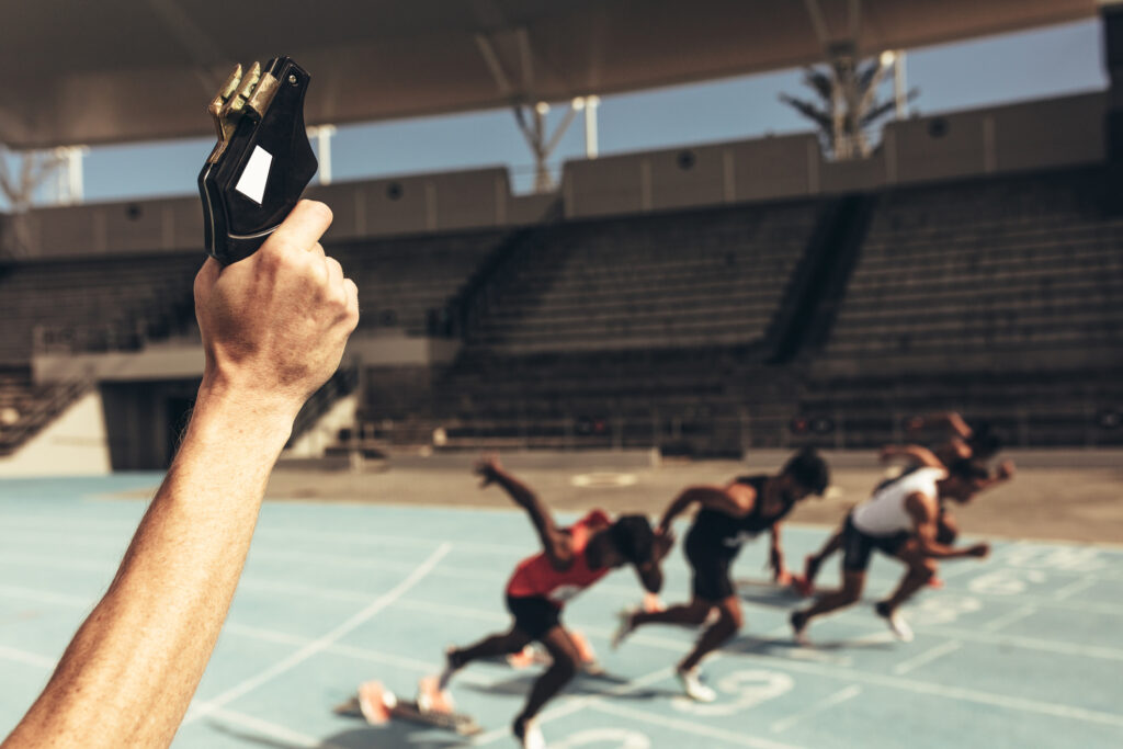 Close up of hand firing a starter pistol to start the running race. Athletes starting off for a race on a running track.